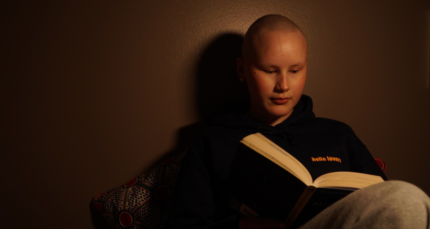 Ung kvinne uten hår leser en bok