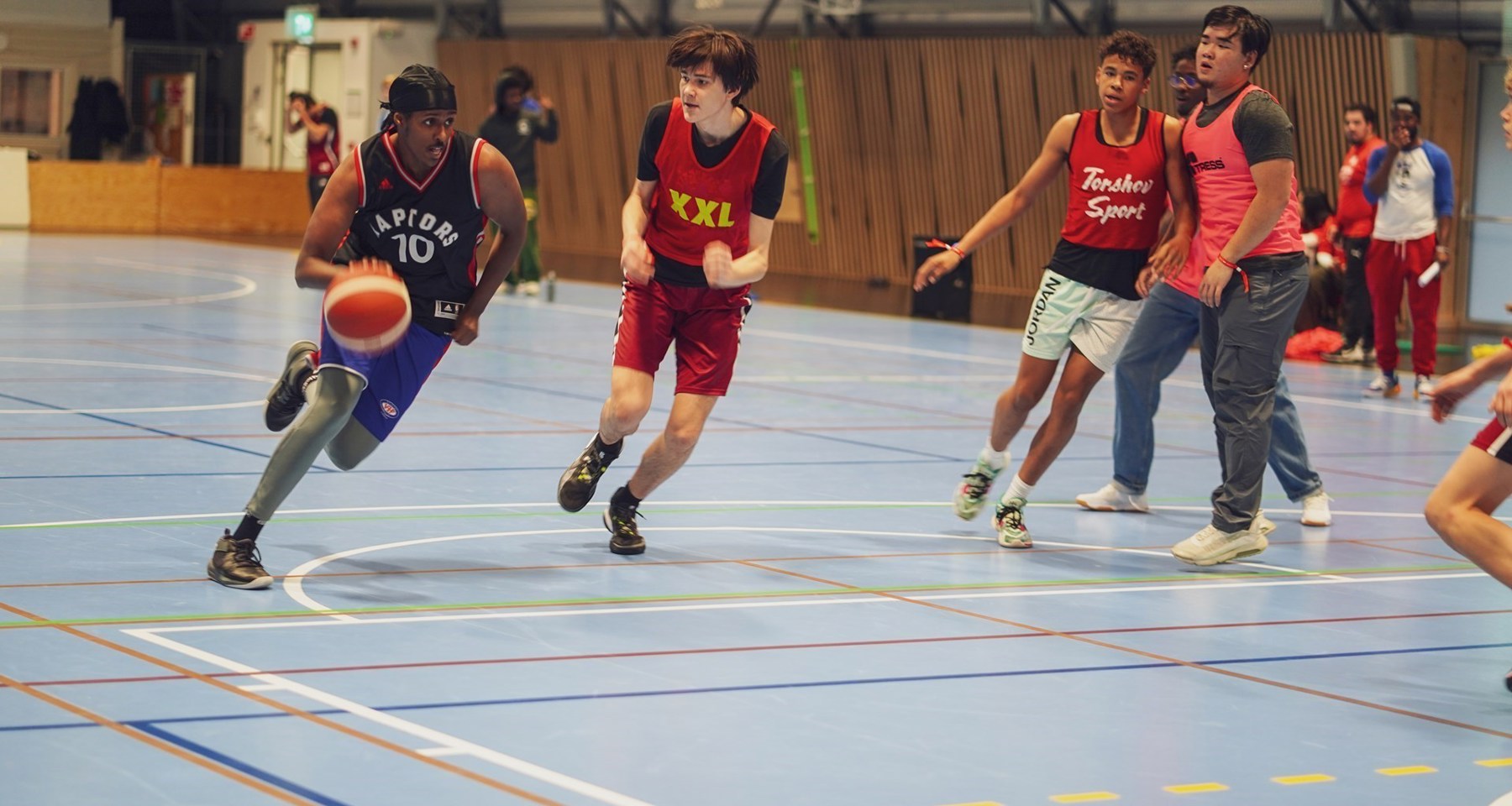 En gruppe ungdommer spiller basketball i en gymsal.
