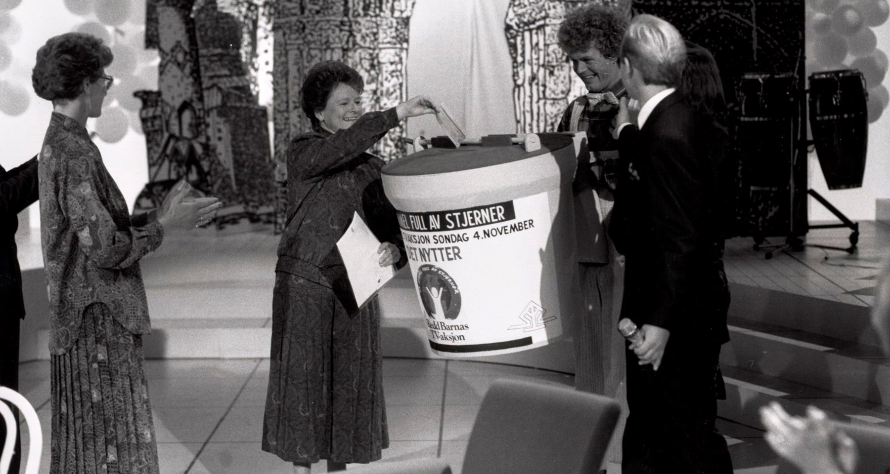 Gro Harlem Brundtland i studio i 1990, gir gave til TV-aksjonen på vegne av regjeringen. Hun putter en sjekk i en stor bøsse, og får applaus av folk rundt.